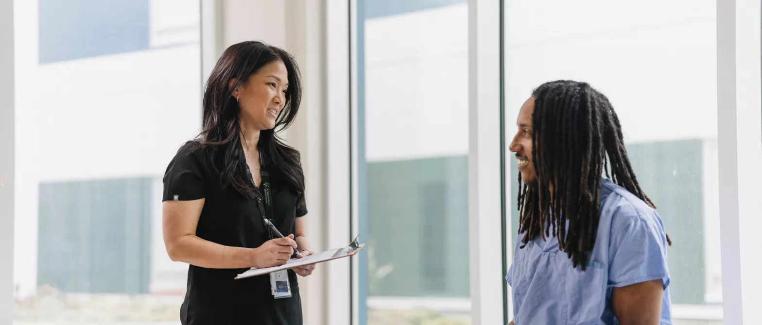Female doctor standing talking to seated patient