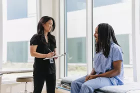 Female doctor standing talking to seated patient
