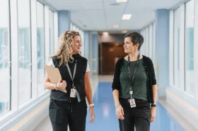 Two staff members walking down corridor and smiling