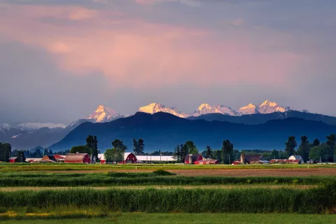Snow-capped mountains under a pink sky backdrop with red barns