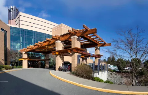 Hospital entrance with a large wooden pergola, glass windows, and bike rack