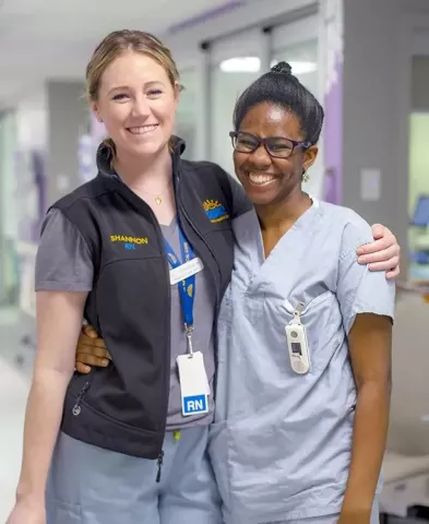 Two smiling nurses with arms around each other's shoulders