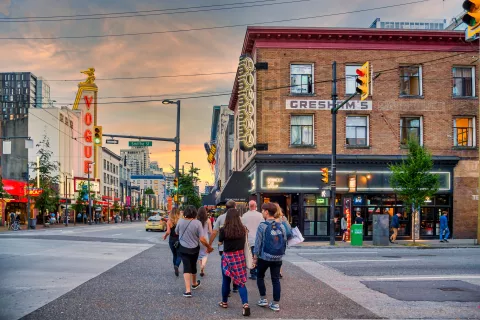 Street scene at sunset with people walking and a vibrant atmosphere, including a prominent "Vogue" sign