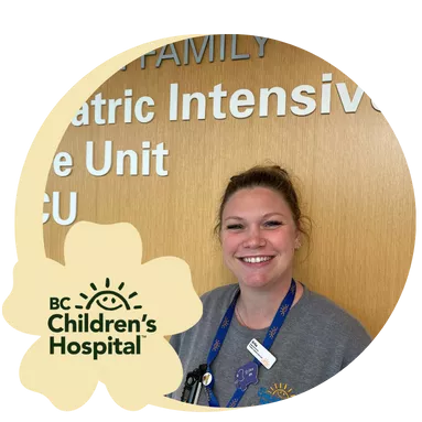 Smiling woman in gray scrubs stands in front of a wood wall labeled "Hudson Family Pediatric Intensive Care Unit PICU"