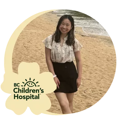 Smiling woman stands on a sandy beach, wearing a floral blouse, dark skirt and sneakers