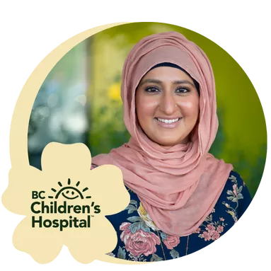 A woman in a floral dress and pink hijab smiles warmly against a blurred green background