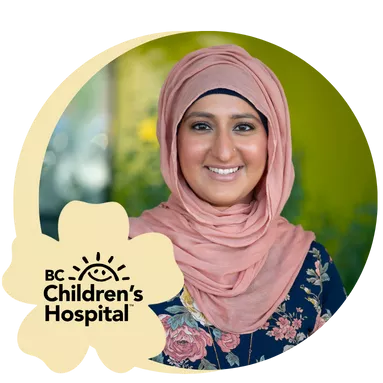 A woman in a floral dress and pink hijab smiles warmly against a blurred green background