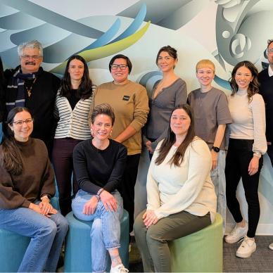 A group of eleven people pose cheerfully in front of a vibrant abstract mural